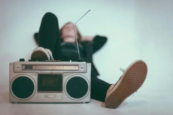 Osoba relaksuje się przy radiomagnetofonie, słuchając muzyki. To pokazuje, jak łatwo dotrzeć do odbiorców, co jest jedną z **zalet reklamy radiowej**.