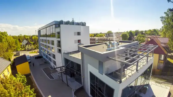 Nowoczesny budynek, gdzie hotel skal właściciel dba o komfort gości. Widać parking, zielone otoczenie i słoneczne niebo.