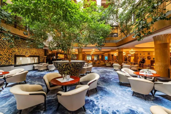 Luksusowy hol hotelowy z bujną roślinnością, wygodnymi fotelami i ozdobnym dywanem. Idealne miejsce na relaks w sieci luksusowych hoteli.